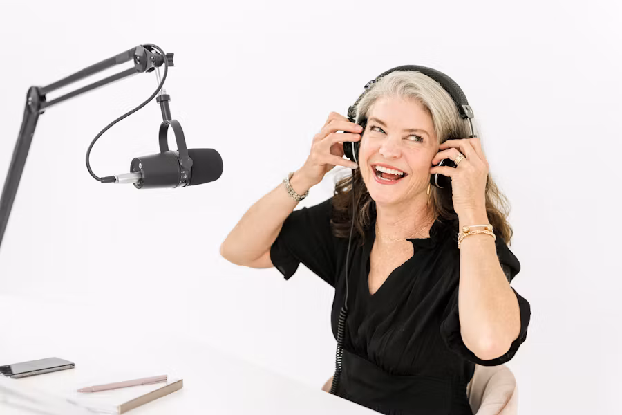 A smiling woman putting on studio headphones next to a podcast microphone